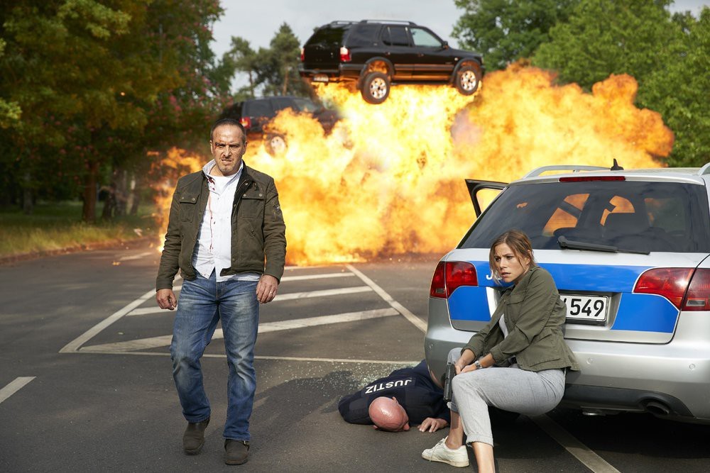 Sami part et Jenny se protège derrière une voiture pendant qu'un SUV explose