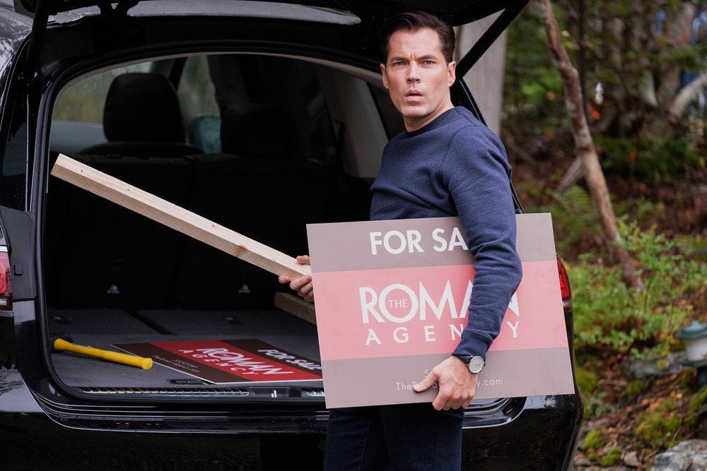 Luke Roman (Tim Rozon) range le panneau de l'agence dans sa voiture