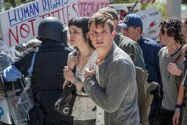 Roman (Matt Lanter) & Sophia (Brina Palencia) traversent la foule de manifestants anti extra-terrestre.